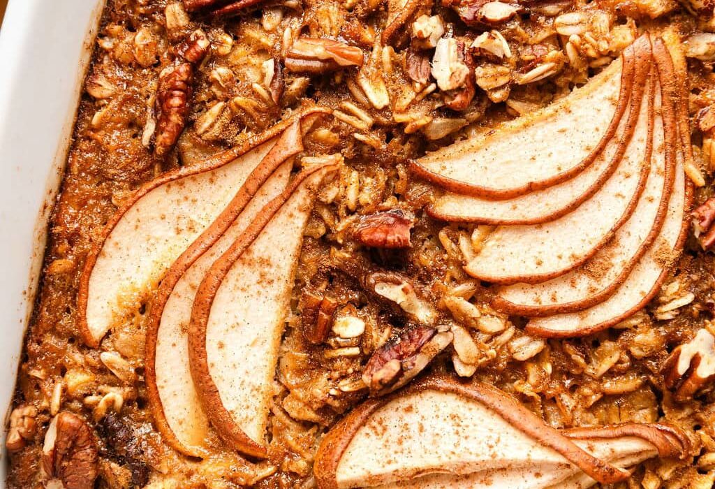 Close up view of a white baking dish filled with Gingerbread Baked Oatmeal topped with thinly sliced pears and pecan pieces.