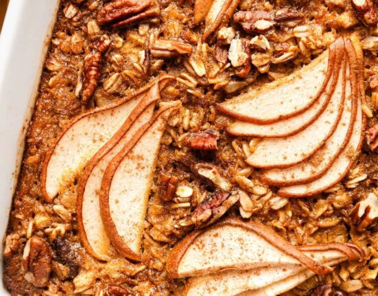 Close up view of a white baking dish filled with Gingerbread Baked Oatmeal topped with thinly sliced pears and pecan pieces.
