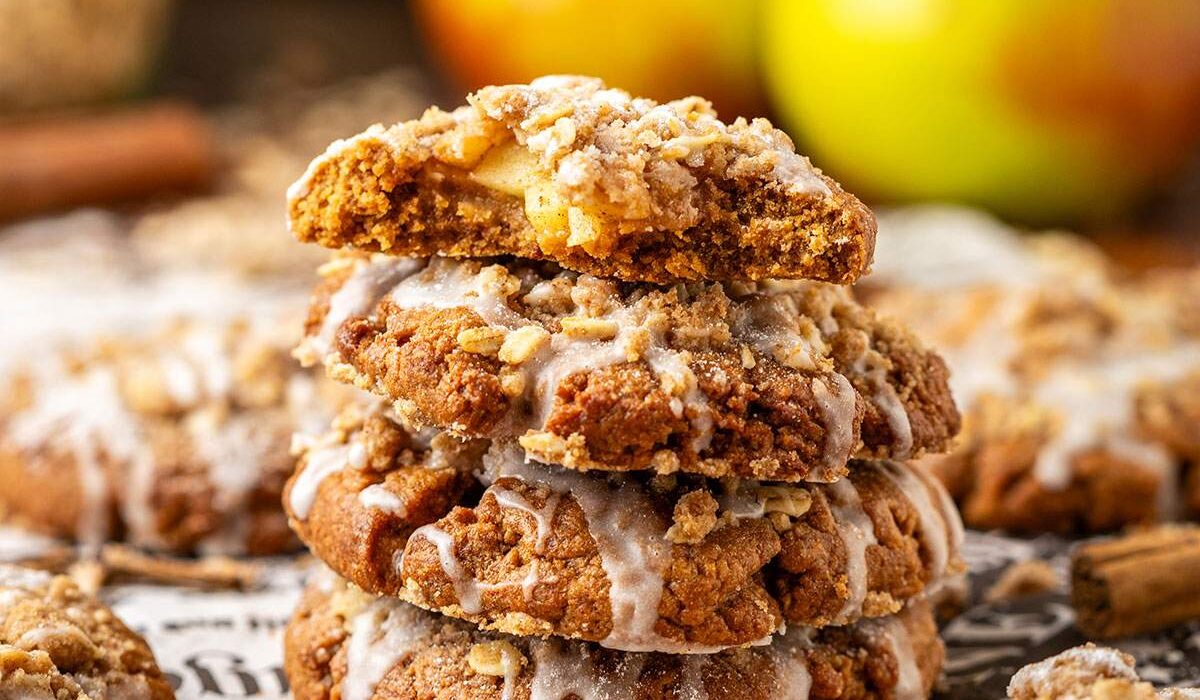 Four stacked apple cookies with glaze, and a bite taken out of the cookie on top, showing the apple filling.