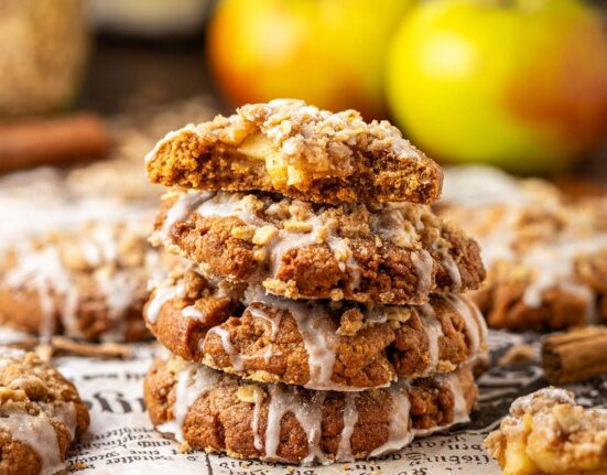 Four stacked apple cookies with glaze, and a bite taken out of the cookie on top, showing the apple filling.