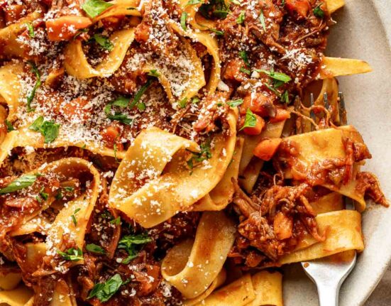 Close up view of a plate of Oven-Braised Beef Ragu topped with parmesan cheese and fresh herbs.