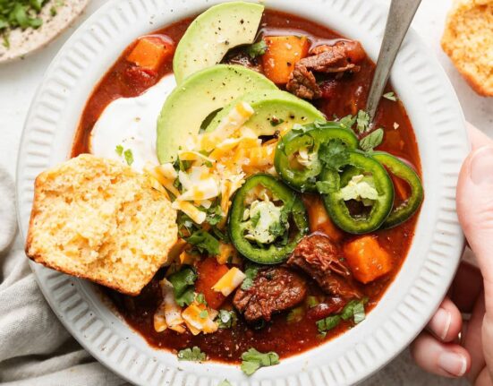 Overhead view of a bowl of Slow Cooker Chuck Roast Chili With Sweet Potatoes and a corn bread muffin on the side.
