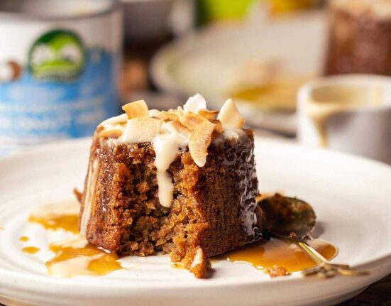 Individual sticky toffee pudding served on a white plate with coconut custard.