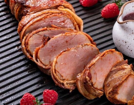 Close Up image of bacon wrapped pork tenderloin with raspberries next to it