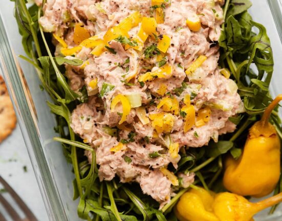 Overhead view of a glass meal prep container filled with arugula and topped with Tuna Salad garnished with pickled peppers.