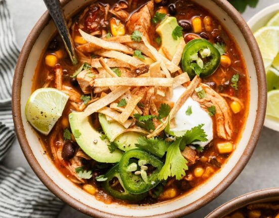 Overhead view of a bowl filled with Chicken Tortilla Soup topped with sliced jalapenos, avocado, and fresh cilantro.