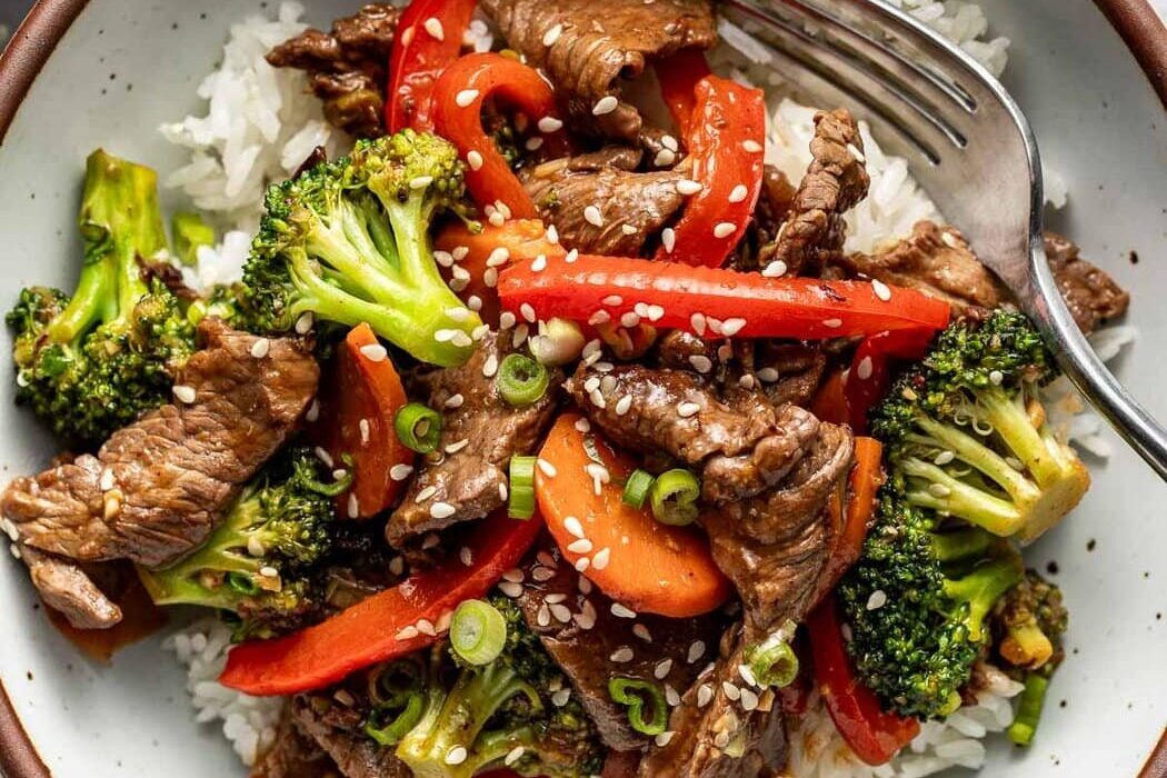Overhead view of a plate of Steak Stir Fry over white rice and topped with sesame seeds.