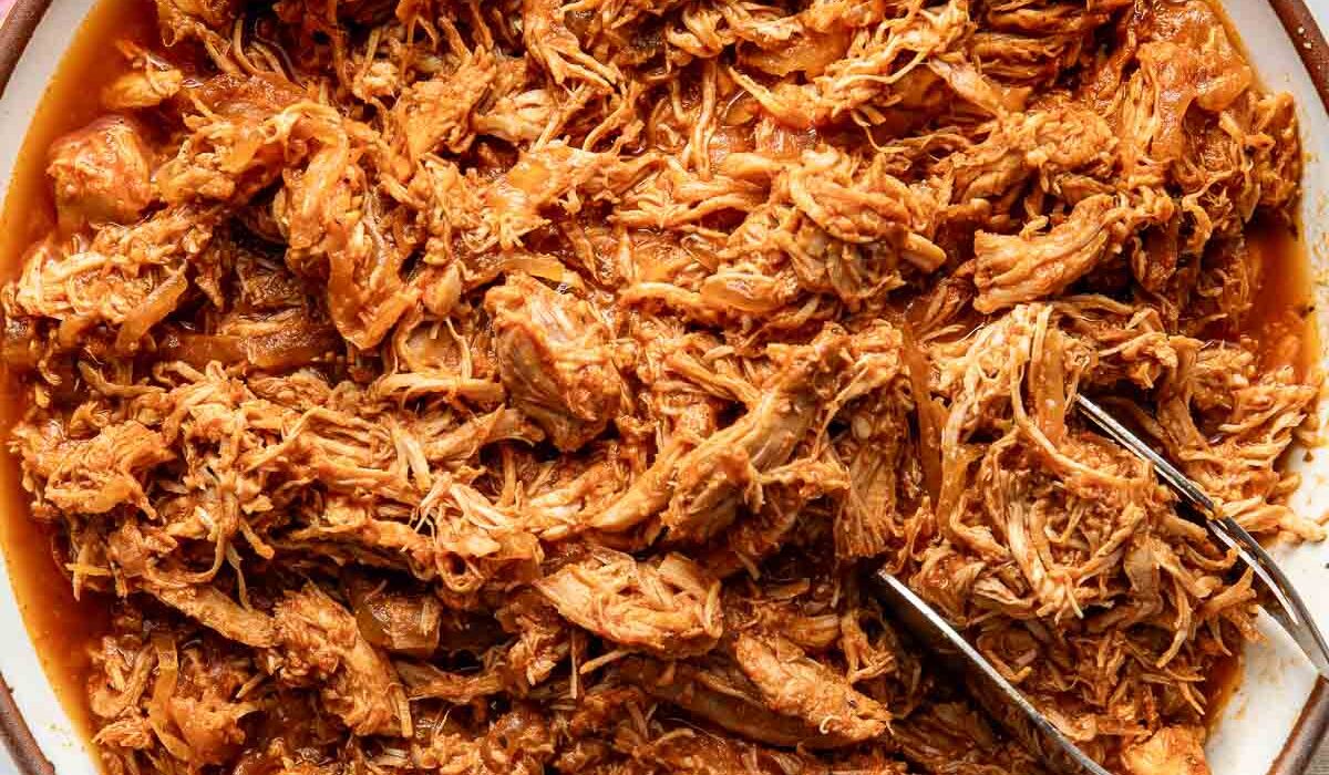Overhead view of a bowl of BBQ Pulled Chicken with a tong on the side for serving.