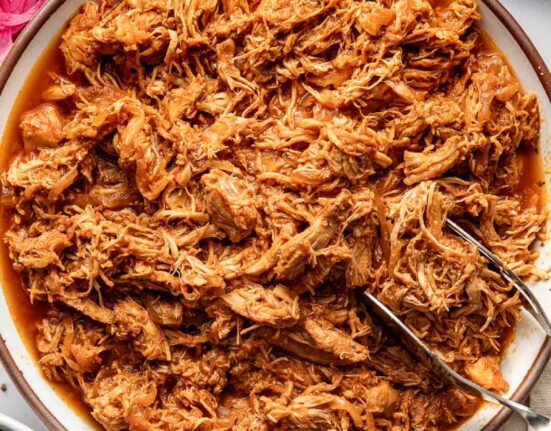 Overhead view of a bowl of BBQ Pulled Chicken with a tong on the side for serving.