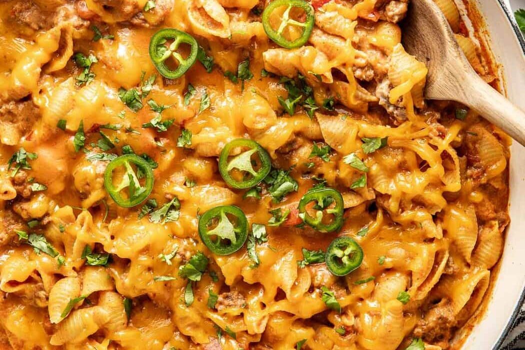 Overhead view of a white skillet filled with Taco Pasta topped with melted cheese and sliced jalapenos.