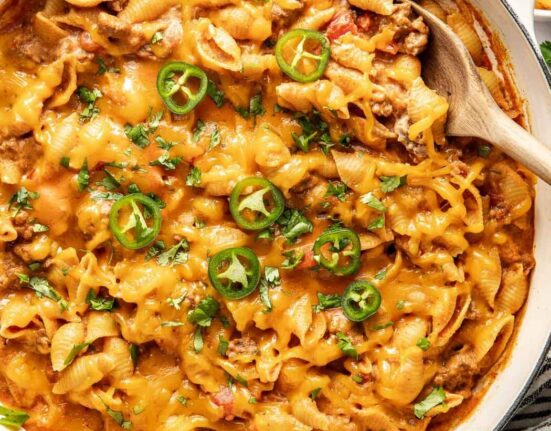 Overhead view of a white skillet filled with Taco Pasta topped with melted cheese and sliced jalapenos.