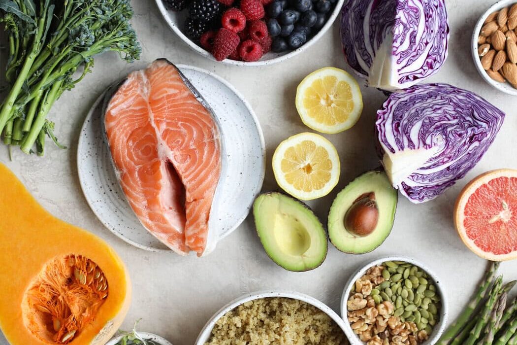 Overhead view of a variety of fruits, vegetables, and salmon on a marble countertop.
