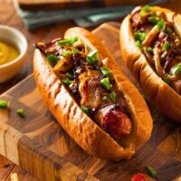 two air fryer bacon wrapped hot dogs on a wooden cutting board