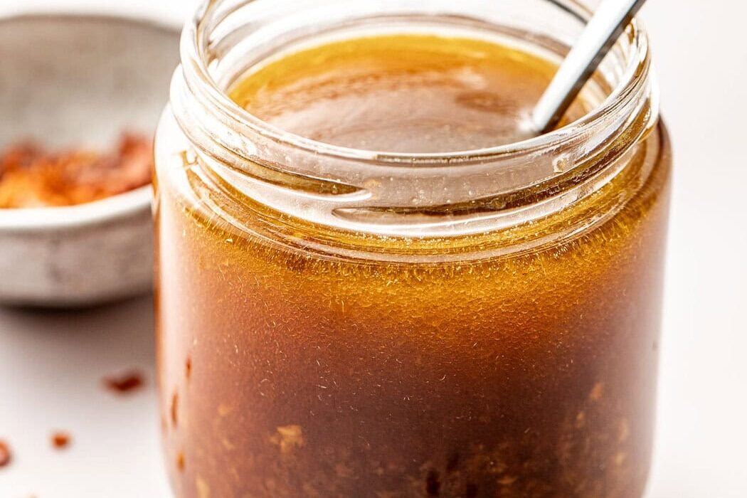 Close up view of a glass jar of Asian Salad Dressing with a spoon stuck into the jar.