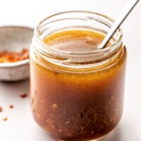 Close up view of a glass jar of Asian Salad Dressing with a spoon stuck into the jar.