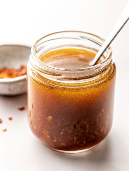 Close up view of a glass jar of Asian Salad Dressing with a spoon stuck into the jar.