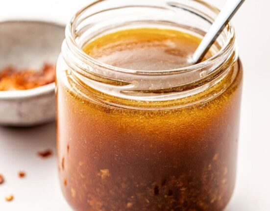 Close up view of a glass jar of Asian Salad Dressing with a spoon stuck into the jar.