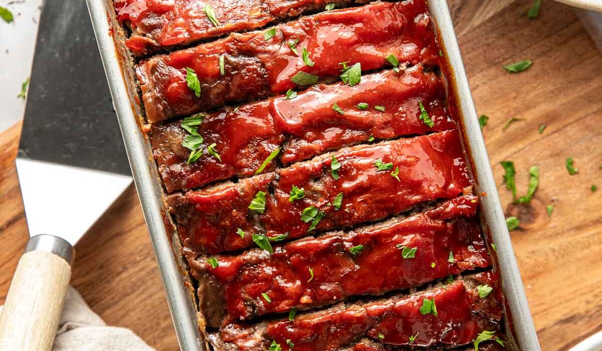 Overhead view of a loaf pan filled with freshly baked meat loaf topped with a tomato topping and sliced for serving.