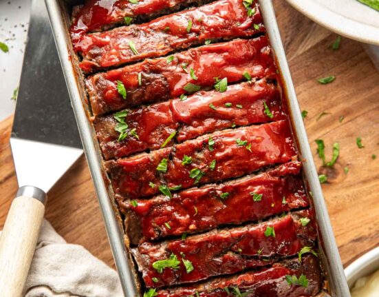 Overhead view of a loaf pan filled with freshly baked meat loaf topped with a tomato topping and sliced for serving.