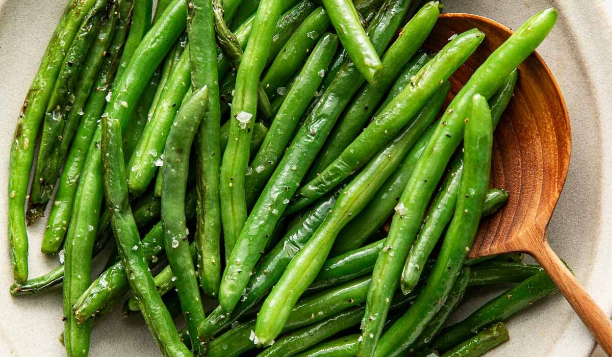 Overhead view of a bowl of Sautéed Green Beans topped with salt and pepper and garnished with a lemon wedge.