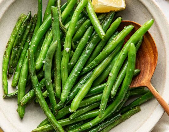 Overhead view of a bowl of Sautéed Green Beans topped with salt and pepper and garnished with a lemon wedge.