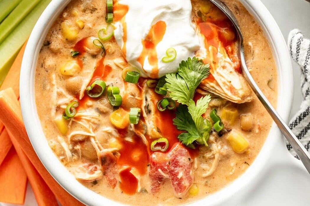 Overhead view of a bowl of Buffalo Chicken Chili topped with green onions and a dollop of sour cream