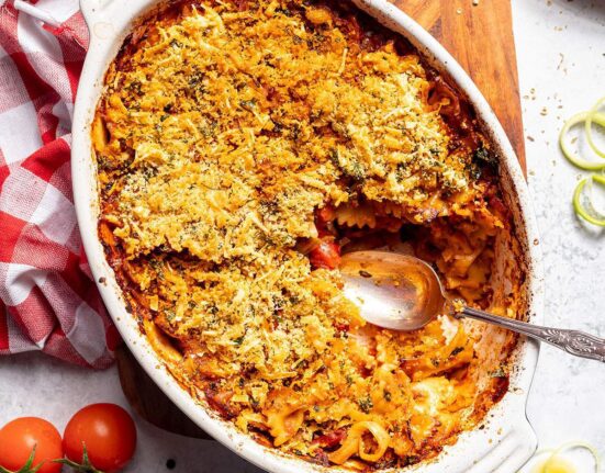 A casserole dish filled with vegan pasta bake and a serving spoon on the side.