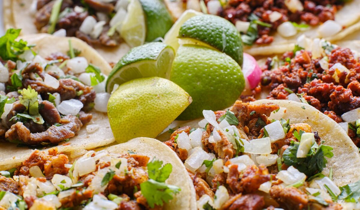 Overhead image of a variety of tacos on a plate with limes in the middle