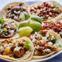 Overhead image of a variety of tacos on a plate with limes in the middle