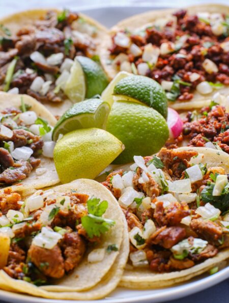 Overhead image of a variety of tacos on a plate with limes in the middle