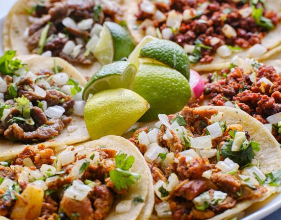Overhead image of a variety of tacos on a plate with limes in the middle