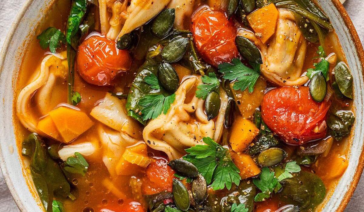 A bowl of vegan tortellini soup with fresh parsley on top.