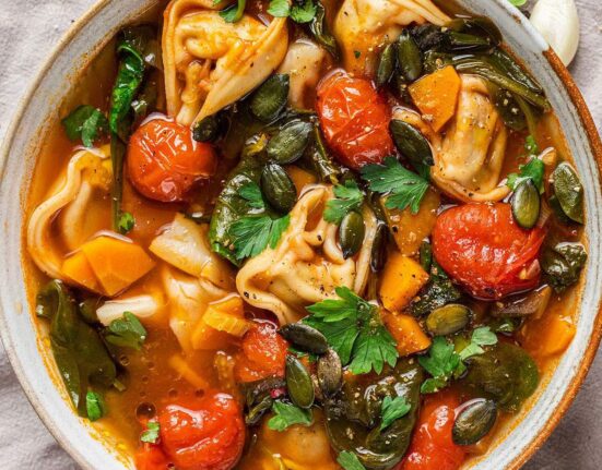 A bowl of vegan tortellini soup with fresh parsley on top.