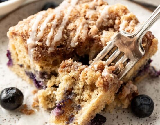Close up view of a piece of Blueberry Coffee Cake with a fork going into the side drizzled with icing on top.