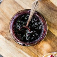 Overhead image of Blueberry Compote in a glass jar with a serving spoon