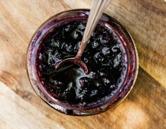 Overhead image of Blueberry Compote in a glass jar with a serving spoon