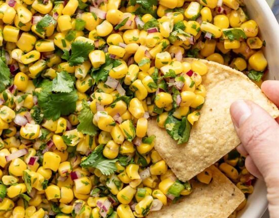Overhead view of a bowl of Copycat Chipotle Corn Salsa with a hand scooping a tortilla chip into the mixture.