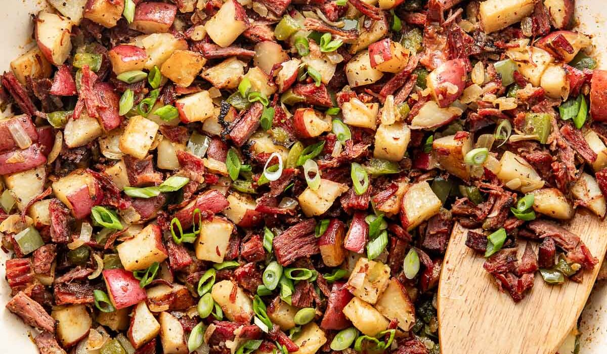 Overhead view of a white skillet filled with Corned Beef Hash topped with green onions.