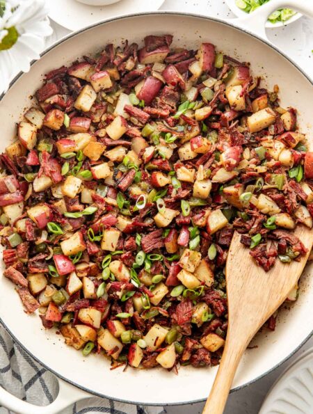 Overhead view of a white skillet filled with Corned Beef Hash topped with green onions.
