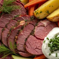 overhead image of sliced and seasoned corned beef on a plate with potatoes, carrots, and sauce