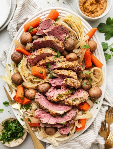 Overhead view of a platter of Crockpot Corned Beef and Cabbage with carrots and fresh herbs.