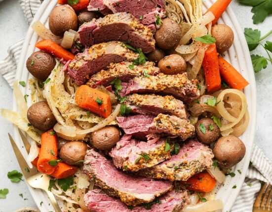 Overhead view of a platter of Crockpot Corned Beef and Cabbage with carrots and fresh herbs.