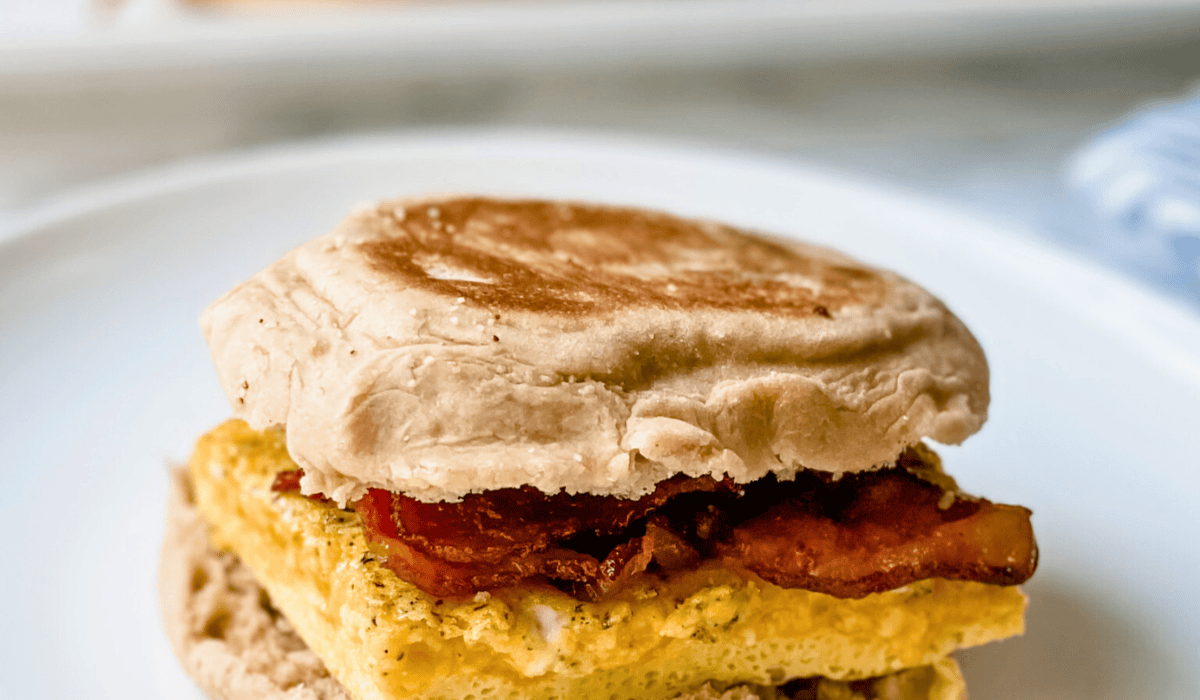 Close-up picture or egg, bacon and cheese breakfast sandwich on a white plate.