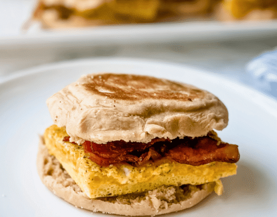 Close-up picture or egg, bacon and cheese breakfast sandwich on a white plate.