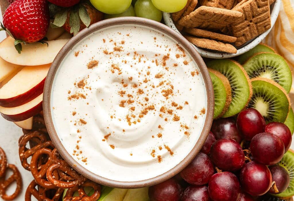 Overhead view of a variety of colorful fruit with a bowl of creamy fruit dip in the middle sprinkled with cinnamon.