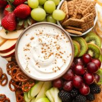 Overhead view of a variety of colorful fruit with a bowl of creamy fruit dip in the middle sprinkled with cinnamon.