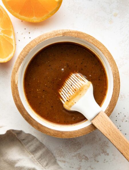 Overhead view of a small dish filled with Ham Glaze mixture next to sliced oranges.