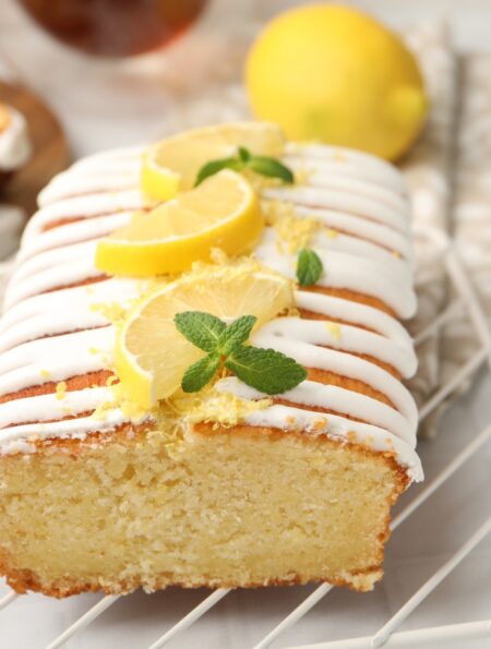 Close up image of lemon yogurt cake on a cooling rack with sliced lemon garnish