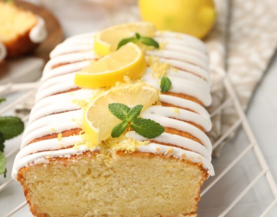 Close up image of lemon yogurt cake on a cooling rack with sliced lemon garnish