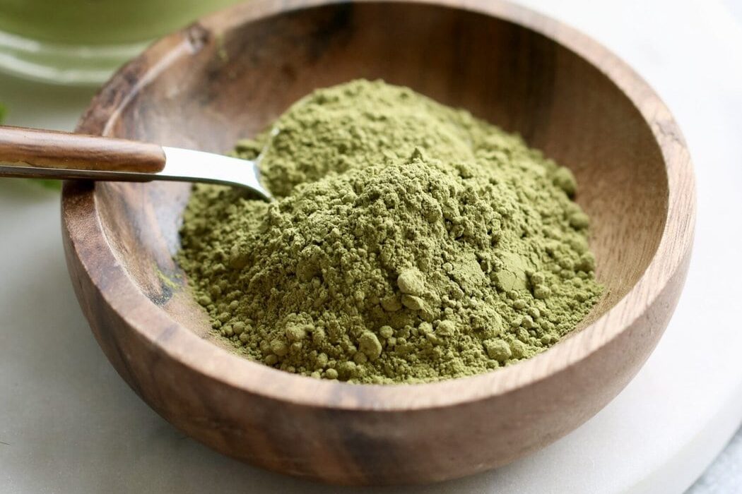 Close up view of a small wooden dish filled with green matcha powder with a spoon stuck into the powder.